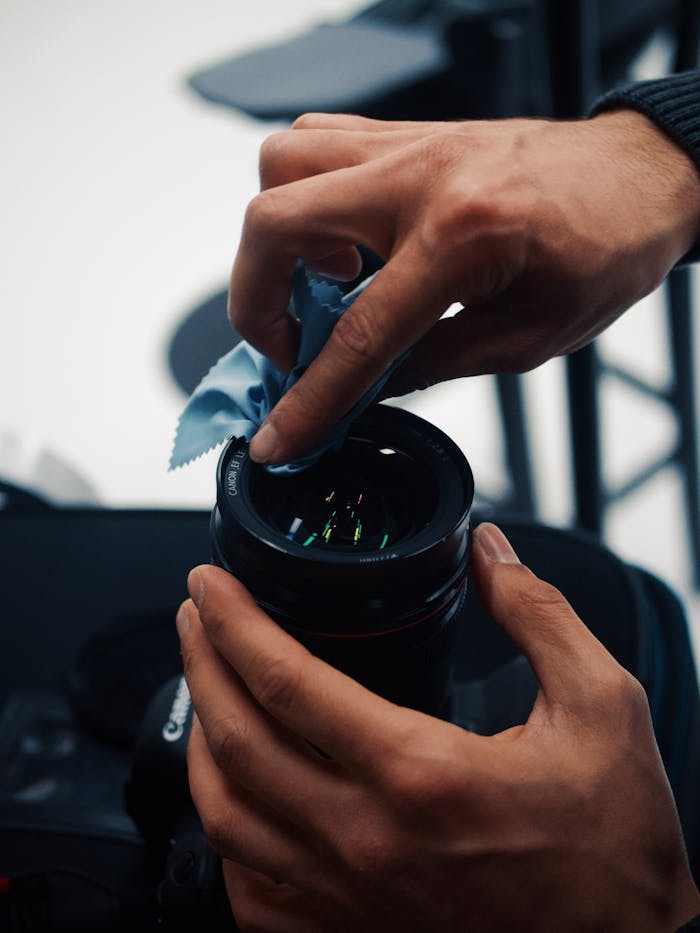 Hands expertly cleaning a camera lens with a blue cloth indoors.